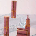 Pink glittery lipsticks with gold accents on a reflective surface