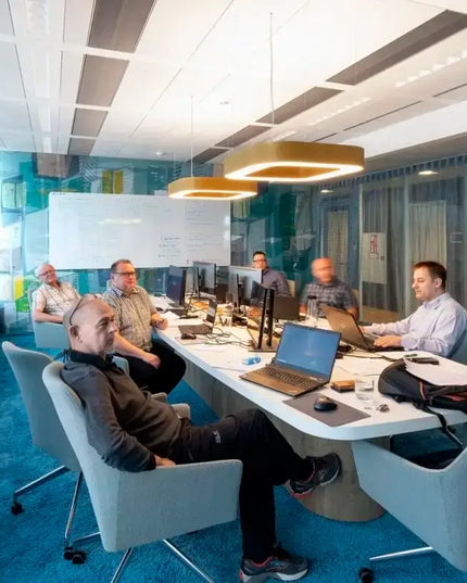 Group of colleagues in a modern office space engaged in a meeting with computers and collaborative tools.