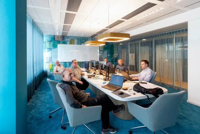 Group of colleagues in a modern office space engaged in a meeting with computers and collaborative tools.