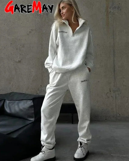 Person wearing a white tracksuit with 'GAREMAY' branding against a gray wall.