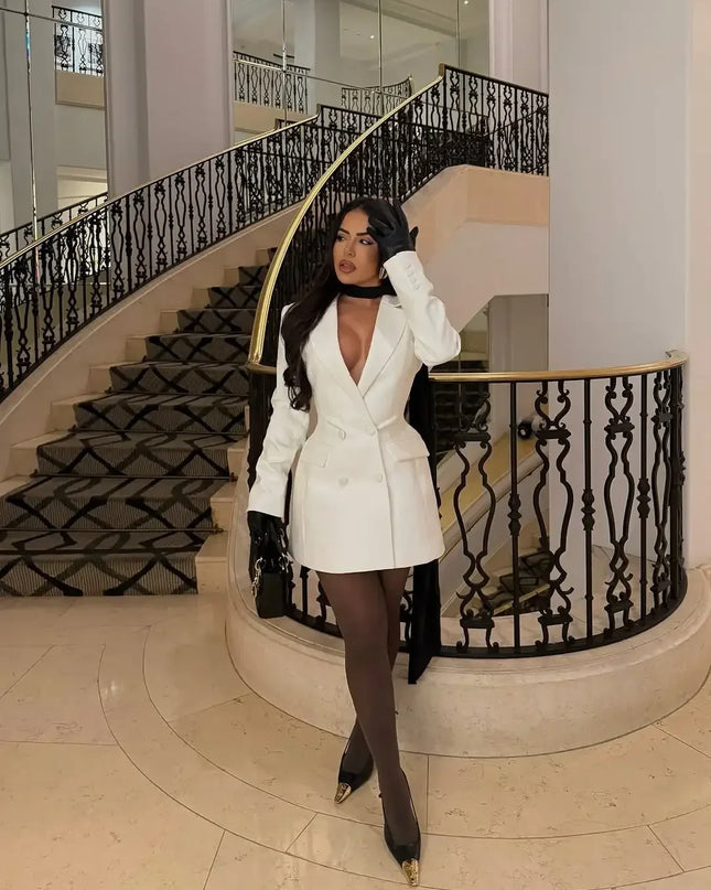 Woman in a white coat standing in a grand staircase interior.