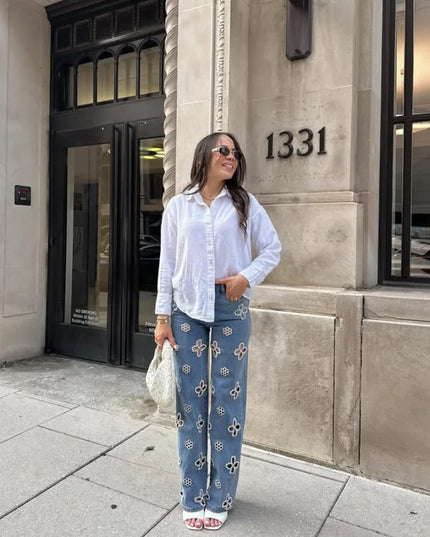 Casual hollow out women’s jeans paired with a white shirt, standing stylishly outside a building.