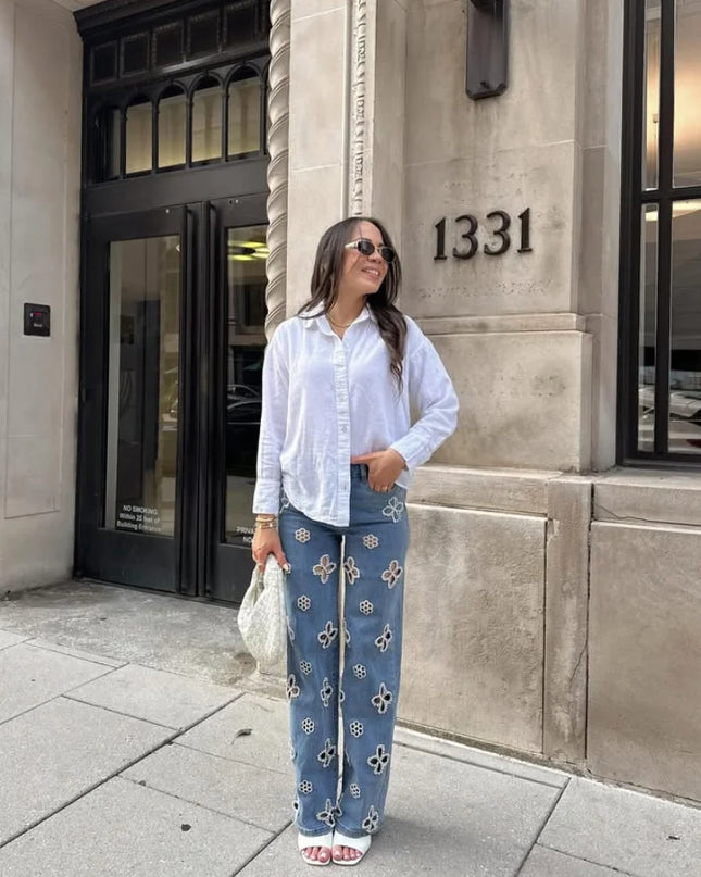 Casual hollow out women’s jeans paired with a white shirt, standing stylishly outside a building.