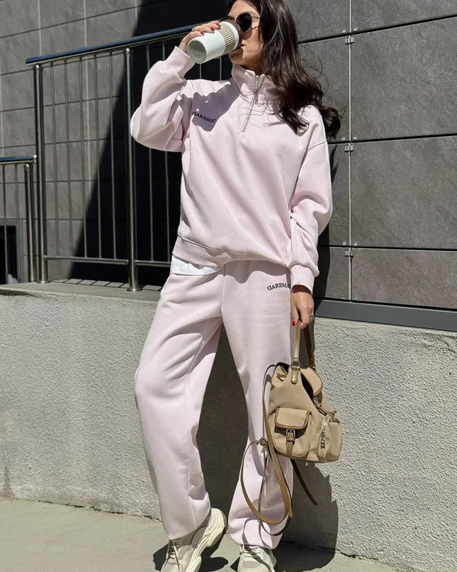 Person wearing a pink tracksuit with a beige backpack against a gray wall.