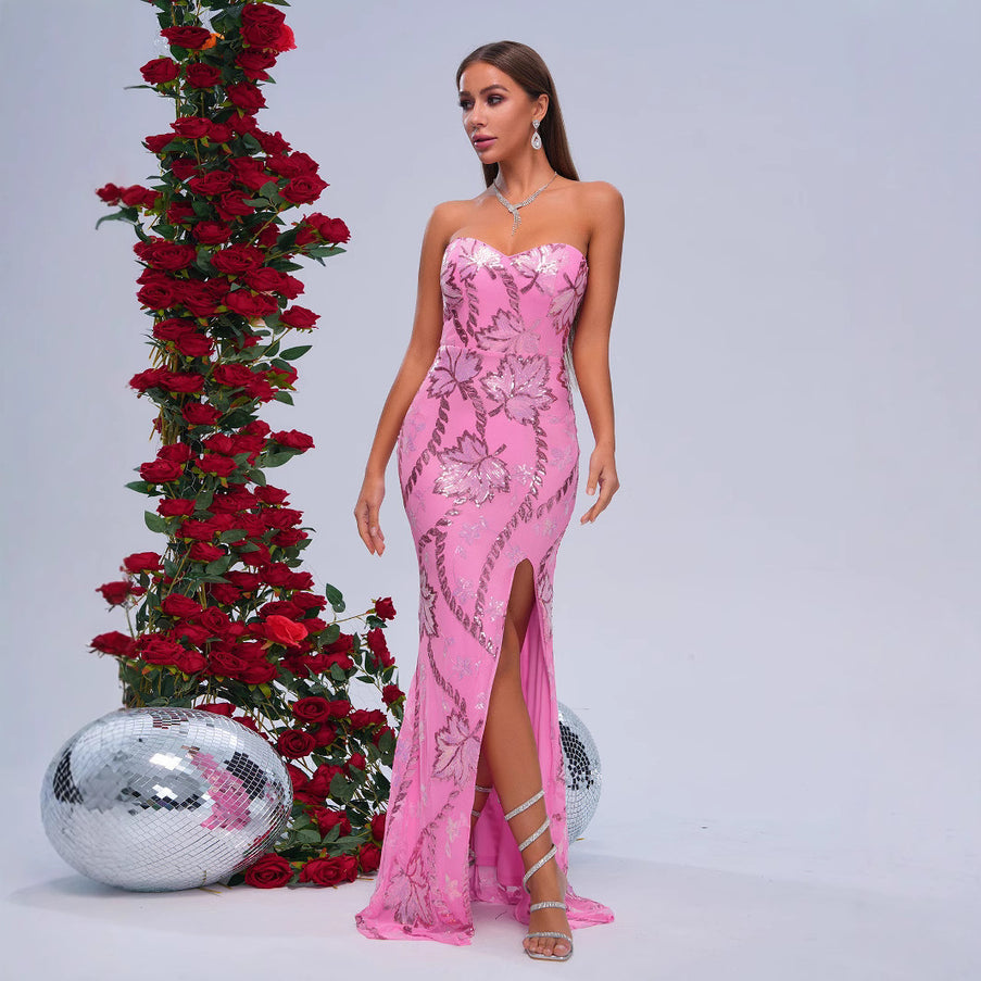 Woman in a pink evening gown standing next to a decorative arrangement of red roses and a disco ball on a light gray background.
