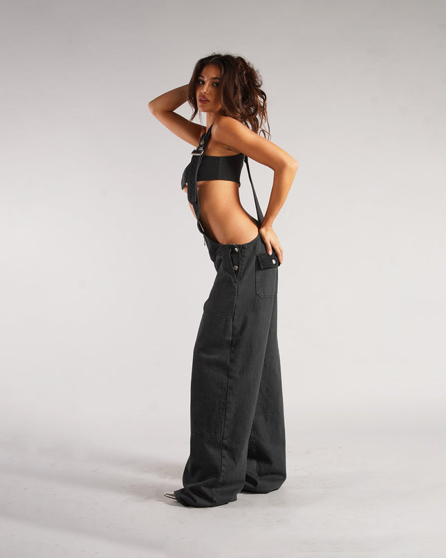 Woman wearing black suspenders and wide-leg jeans on a plain background